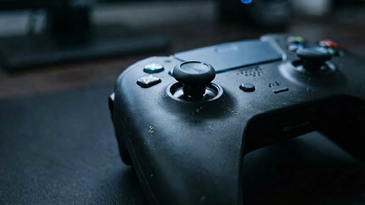 Close-up of a game controller left analog stick in dim blue-grey light, worn stick on a dark desk